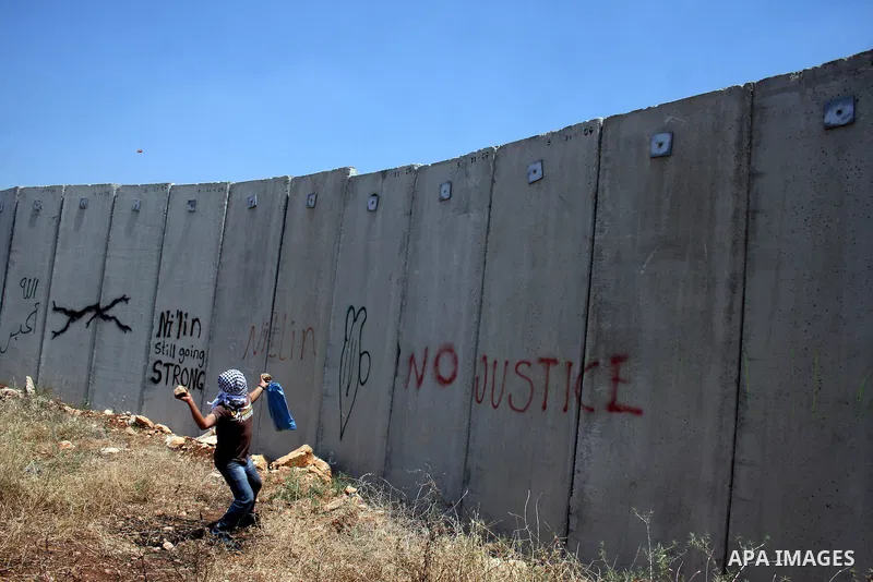 A Palestinian demonstrator throws stones to Israeli troops, not seen, during a protest against Israel's separation barrier in the West Bank village of Nilin, near Ramallah, Friday, June 3, 2011. Photo by Issam Rimawi
