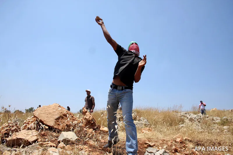 A Palestinian demonstrator throws stones to Israeli troops, not seen, during a protest against Israel's separation barrier in the West Bank village of Nilin, near Ramallah, Friday, June 3, 2011. Photo by Issam Rimawi