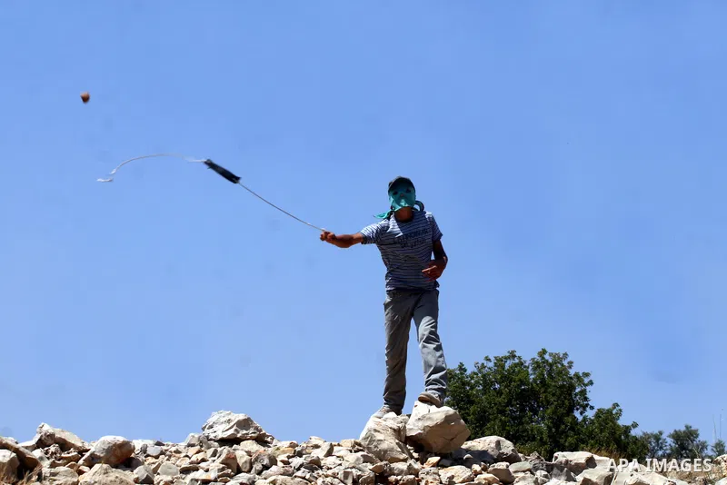 A Palestinian demonstrator throws stones to Israeli troops, not seen, during a protest against Israel's separation barrier in the West Bank village of Nilin, near Ramallah, Friday, June 3, 2011. Photo by Issam Rimawi