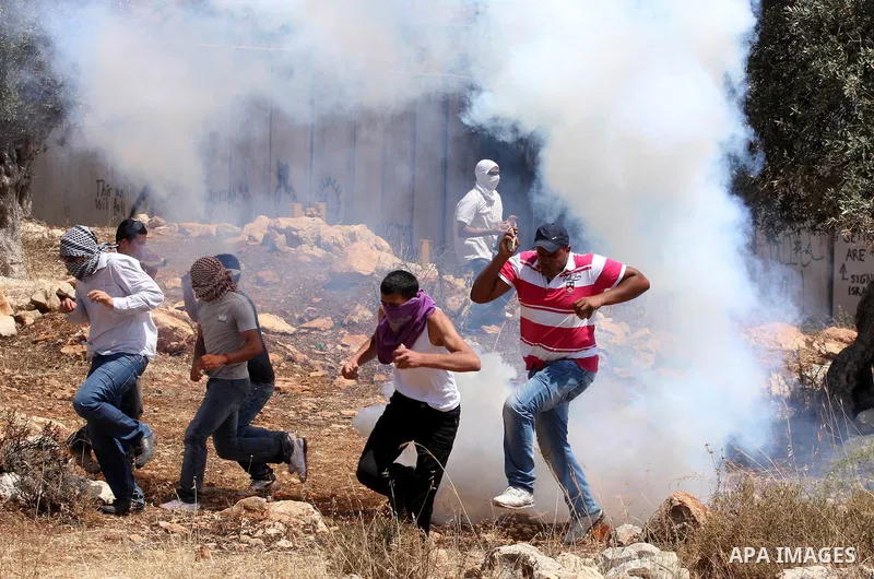 Palestinian demonstrators run for cover from tear gas canisters fired by Israeli soldiers, not seen, during a protest against Israel's separation barrier in the West Bank village of Nilin, near Ramallah, Friday, June 3,...