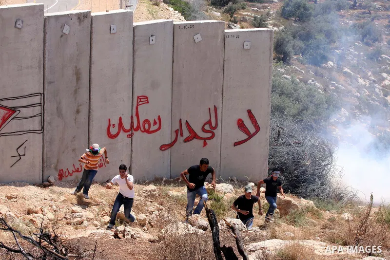 Palestinian demonstrators run for cover from tear gas canisters fired by Israeli soldiers, not seen, during a protest against Israel's separation barrier in the West Bank village of Nilin, near Ramallah, Friday, June 3,...