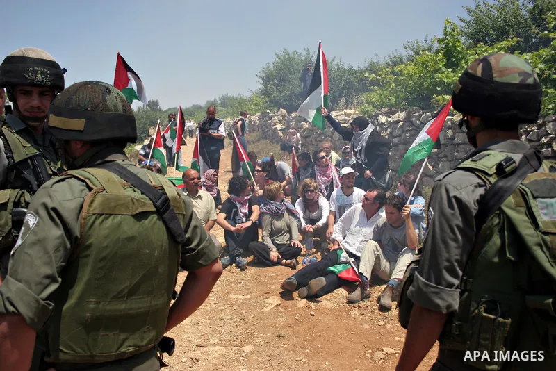 Israeli soldiers stand guard as protesters hold up Palestinian flag during a demonstration by foreign, Israeli and Palestinian activists against the Jewish settlement of Karmei Tzur near the Palestinian village of Beit O...