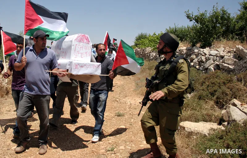 Israeli soldiers stand guard as protesters hold up Palestinian flag during a demonstration by foreign, Israeli and Palestinian activists against the Jewish settlement of Karmei Tzur near the Palestinian village of Beit O...