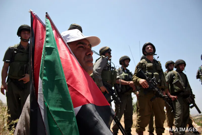 Israeli soldiers stand guard as protesters hold up Palestinian flag during a demonstration by foreign, Israeli and Palestinian activists against the Jewish settlement of Karmei Tzur near the Palestinian village of Beit O...
