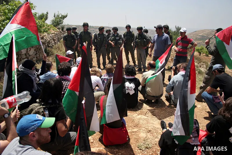 Israeli soldiers stand guard as protesters hold up Palestinian flag during a demonstration by foreign, Israeli and Palestinian activists against the Jewish settlement of Karmei Tzur near the Palestinian village of Beit O...