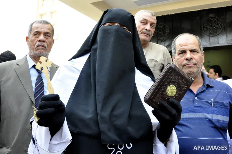 An Egyptian Muslim woman holds a cross with a Koran, Islam's holy book, as she joins Coptic Christians for Sunday mass at the Virgin Mary church in the Imbaba district of the Egyptian capital of Cairo on June 5, 2011 fol...