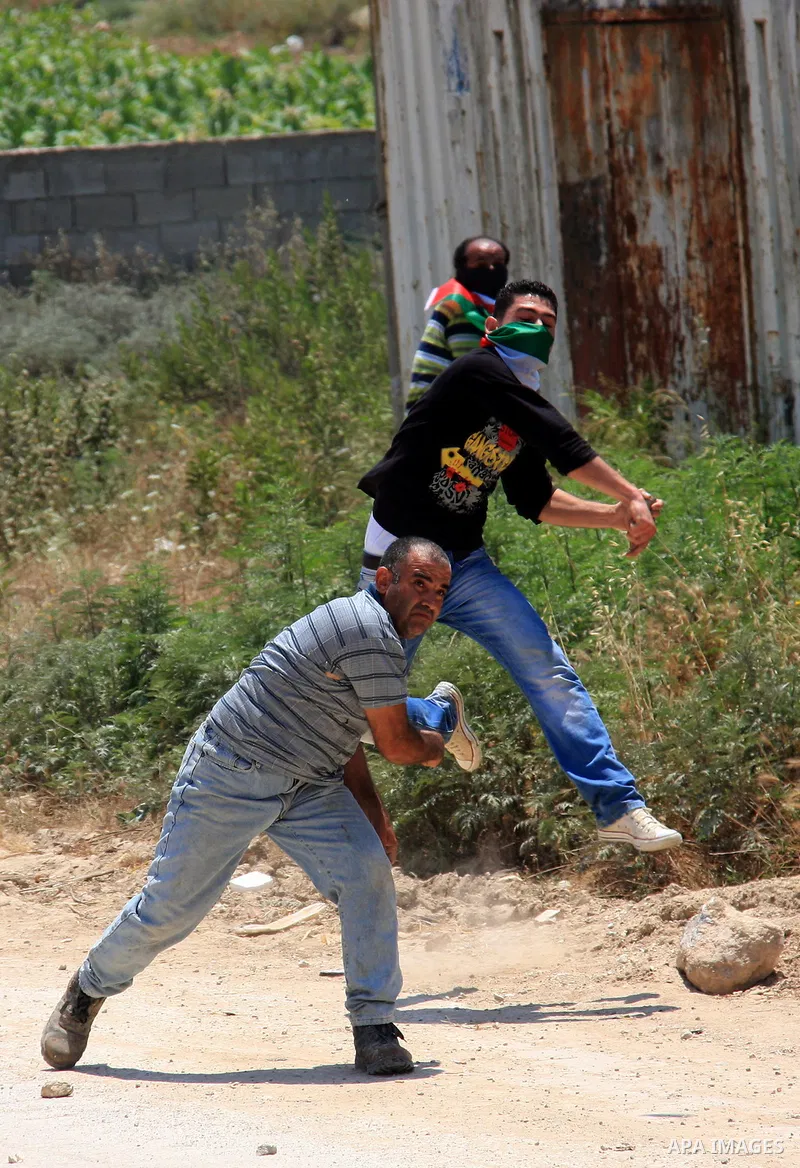 Palestinian youths throw stones at Israeli soldiers following a protest against Israel's separation barrier in the village Nazlet Issa north Tulkarm in the West Bank on June 7, 2011. Photo by Wagdi Eshtayah