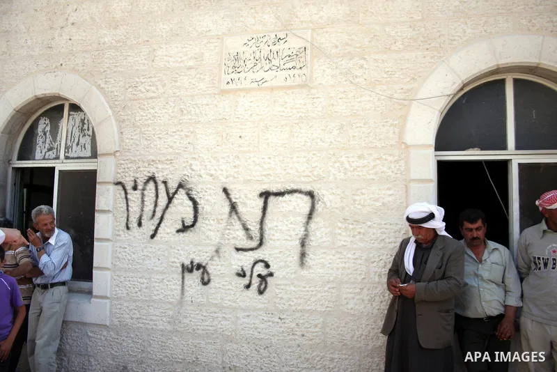 Palestinians stand near graffiti reading in Hebrew: "Price Tag" and "Alei Ayin", which is the name of a nearby Jewish settlement outpost demolished by Israeli police last week, painted on the wall of a mosque which was v...