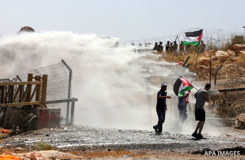A protestor holding the Palestinian national flag runs for cover from coloured water sprayed by Israeli police water cannon vehicle during clashes following a weekly demonstration against Israel's separation barrier in t...