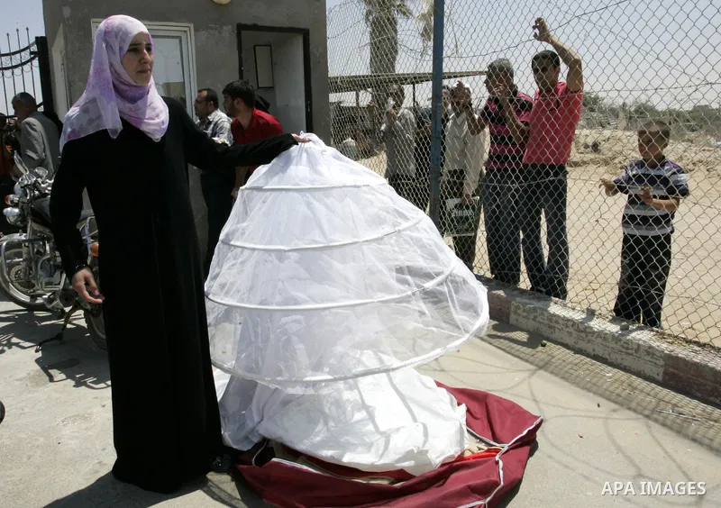 A Palestinian bride and her father display her wedding dress as she waits for authorization to cross the Rafah border crossing with Egypt, in the southern Gaza Strip, on June 21, 2011, and head to Qatar for her wedding....