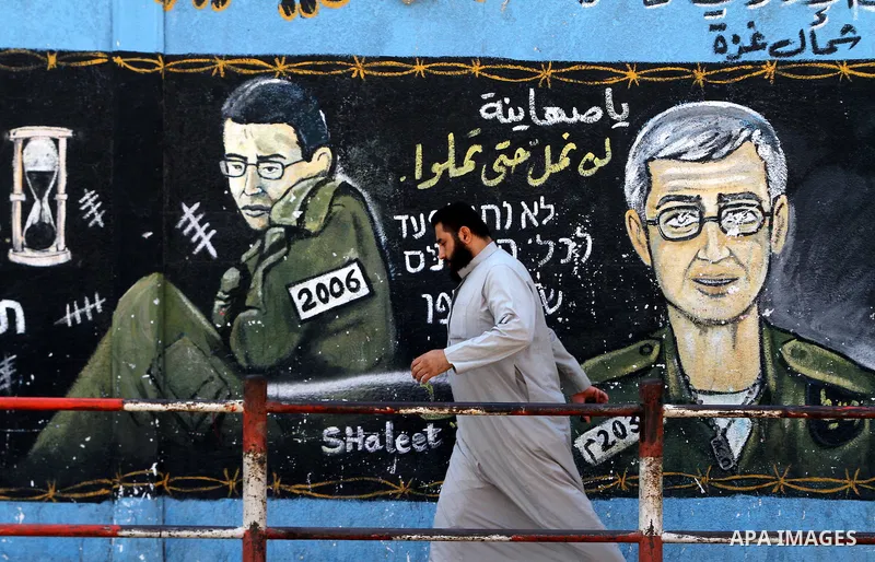 A Palestinian man walks past a mural depicting captured Israeli soldier Gilad Shalit in Jabalya in the northern Gaza Strip June 23, 2011. The Red Cross called on Hamas on Thursday to provide proof that Shalit, captured b...