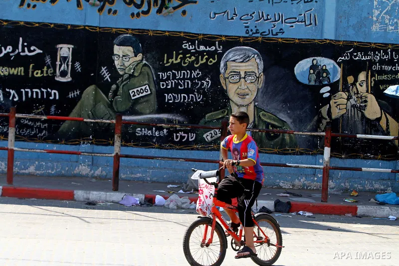 A Palestinian boy rides his bike past a mural depicting captured Israeli soldier Gilad Shalit in Jabalya in the northern Gaza Strip June 23, 2011. The Red Cross called on Hamas on Thursday to provide proof that Shalit, c...