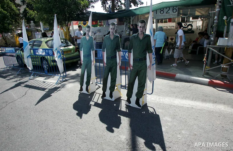 Israelis walk near a cardboard cutout of abducted Israeli soldier Gilad Shalit near Prime Minister Benjamin Netanyahu's residence in Jerusalem on June 25, 2011 as Israelis mark the 1,826th day (5th year) of his captivity...