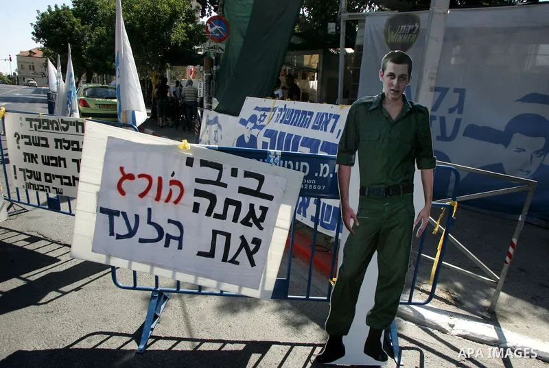 Israelis walk near a cardboard cutout of abducted Israeli soldier Gilad Shalit near Prime Minister Benjamin Netanyahu's residence in Jerusalem on June 25, 2011 as Israelis mark the 1,826th day (5th year) of his captivity...