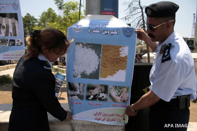Palestinian police officers hold a poster near the confiscated drugs which include heroin, opium and marijuana during a campaign against illegal drugs in the West Bank city of Hebron, 26 June 2011. Photo by Najeh Hashlam...