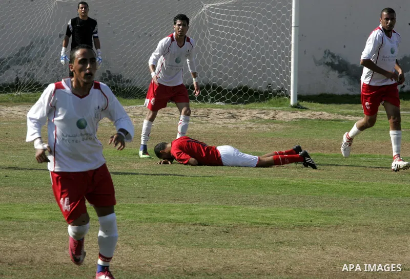 A Palestinian football player falls on the ground during a football match between Khan Yunis Youth club (red shirt) and Rafah Collective club (white shirt) on Jun 27, 2011 in the southern Gaza Strip town of Rafah. Photo...