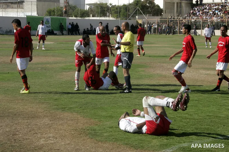 A Palestinian football player falls on the ground during a football match between Khan Yunis Youth club (red shirt) and Rafah Collective club (white shirt) on Jun 27, 2011 in the southern Gaza Strip town of Rafah. Photo...