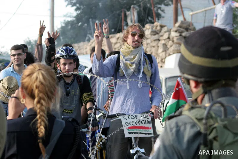 Palestinian and foreign bikers wait behind barbed wire and a cordon of Israeli security forces to ride their bicycles under the slogan of "biking without borders" across a Palestinian road closed off by Israeli troops to...