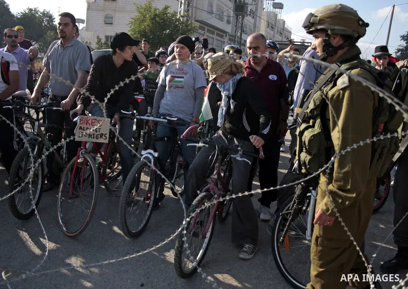 Palestinian and foreign bikers wait behind barbed wire and a cordon of Israeli security forces to ride their bicycles under the slogan of "biking without borders" across a Palestinian road closed off by Israeli troops to...