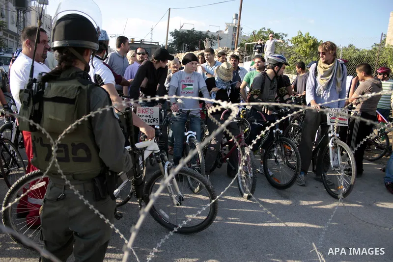 Palestinian and foreign bikers wait behind barbed wire and a cordon of Israeli security forces to ride their bicycles under the slogan of "biking without borders" across a Palestinian road closed off by Israeli troops to...