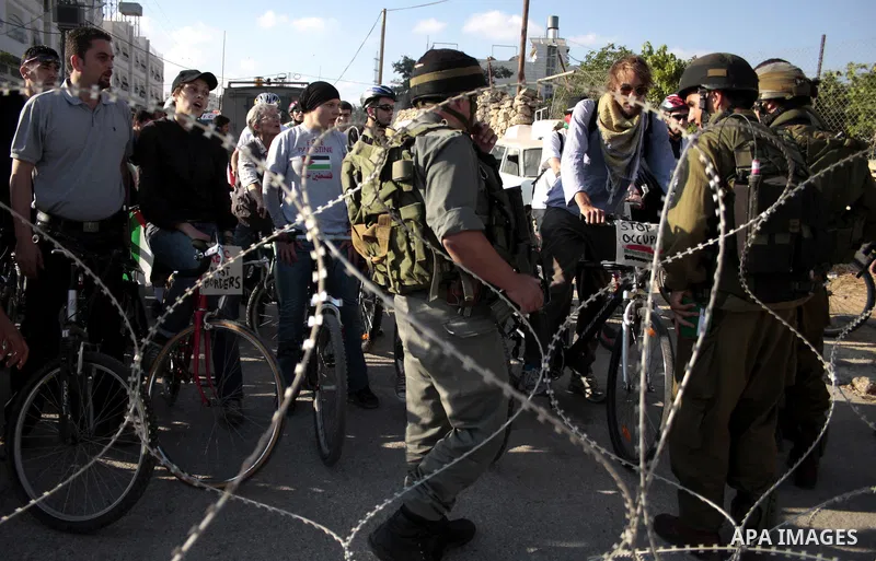 Palestinian and foreign bikers wait behind barbed wire and a cordon of Israeli security forces to ride their bicycles under the slogan of "biking without borders" across a Palestinian road closed off by Israeli troops to...