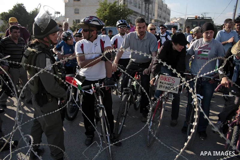 Palestinian and foreign bikers wait behind barbed wire and a cordon of Israeli security forces to ride their bicycles under the slogan of "biking without borders" across a Palestinian road closed off by Israeli troops to...