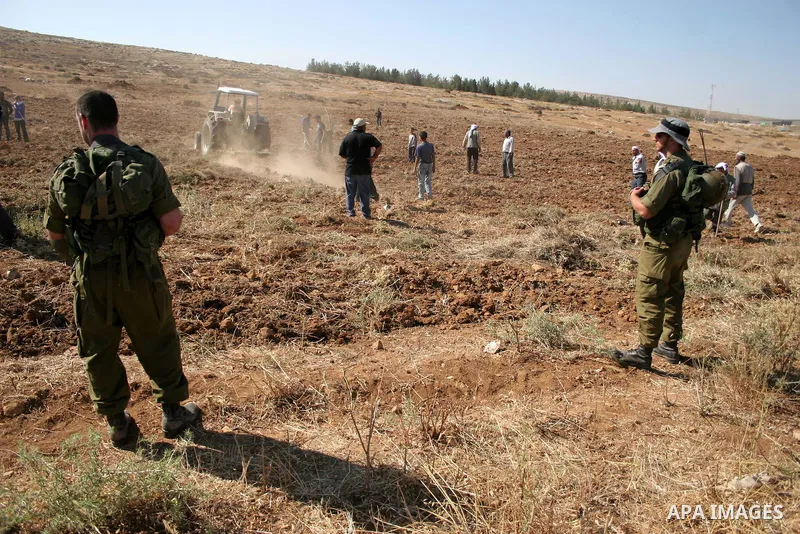 Palestinian farmers work at their land as Israeli border guards prepare to evacuate Jewish settlers who tried to make a sit-in on a Palestinian land that was being cultivated by farmers, on July 1, 2011, in the West Bank...