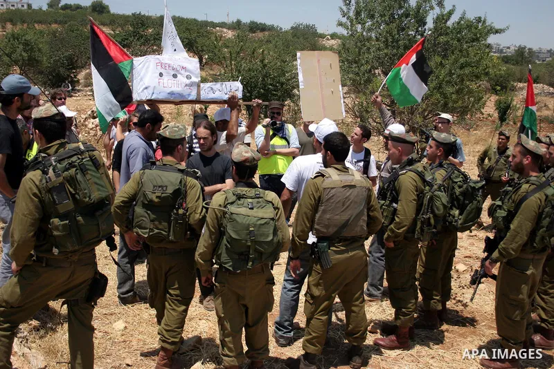Israeli soldiers stand guard as Palestinian, Israeli and foreign activists hold a mock for the Gaza-bound international Freedom Flotilla during a demonstration against the demolishing of farm land to be used in the const...