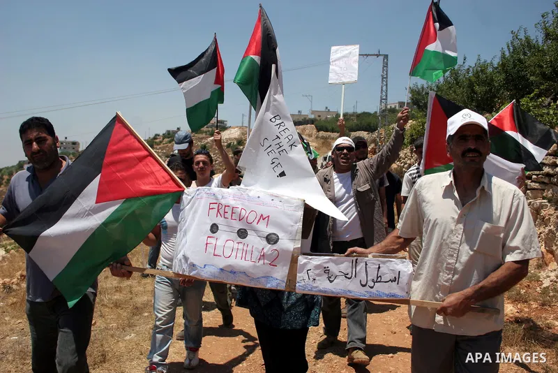 Israeli soldiers stand guard as Palestinian, Israeli and foreign activists hold a mock for the Gaza-bound international Freedom Flotilla during a demonstration against the demolishing of farm land to be used in the const...