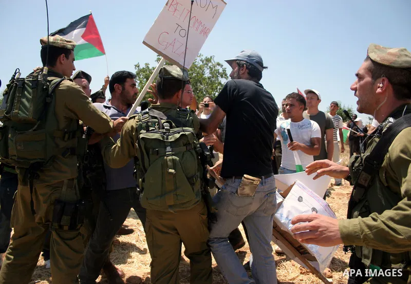 Israeli soldiers scuffle with a protester during a demonstration by Palestinian, Israeli and foreign activists against the demolishing of farm land to be used in the construction of Jewish settlements near the existing I...