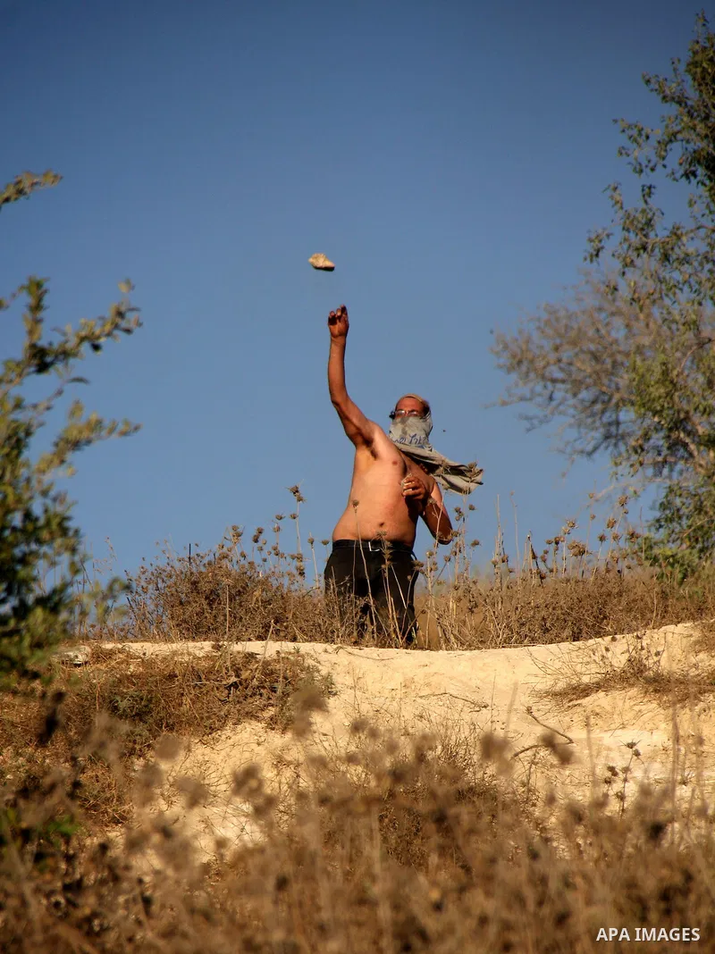 Masked Jewish settlers hurl stones towards Palestinian protesters, during clashes over farming land between the Jewish settlement of Yitzhar and the nearby West Bank village of Asira, near Nablus, Sunday, July 3, 2011. P...