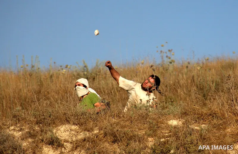 Masked Jewish settlers hurl stones towards Palestinian protesters, during clashes over farming land between the Jewish settlement of Yitzhar and the nearby West Bank village of Asira, near Nablus, Sunday, July 3, 2011. P...