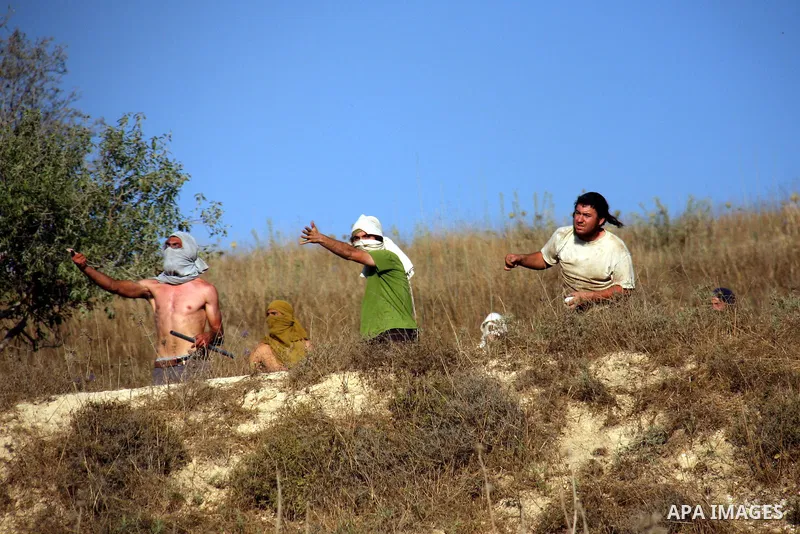 Masked Jewish settlers hurl stones towards Palestinian protesters, during clashes over farming land between the Jewish settlement of Yitzhar and the nearby West Bank village of Asira, near Nablus, Sunday, July 3, 2011. P...