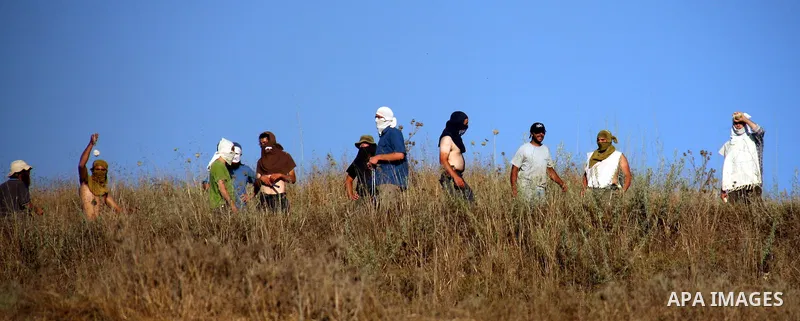 Masked Jewish settlers hurl stones towards Palestinian protesters, during clashes over farming land between the Jewish settlement of Yitzhar and the nearby West Bank village of Asira, near Nablus, Sunday, July 3, 2011. P...