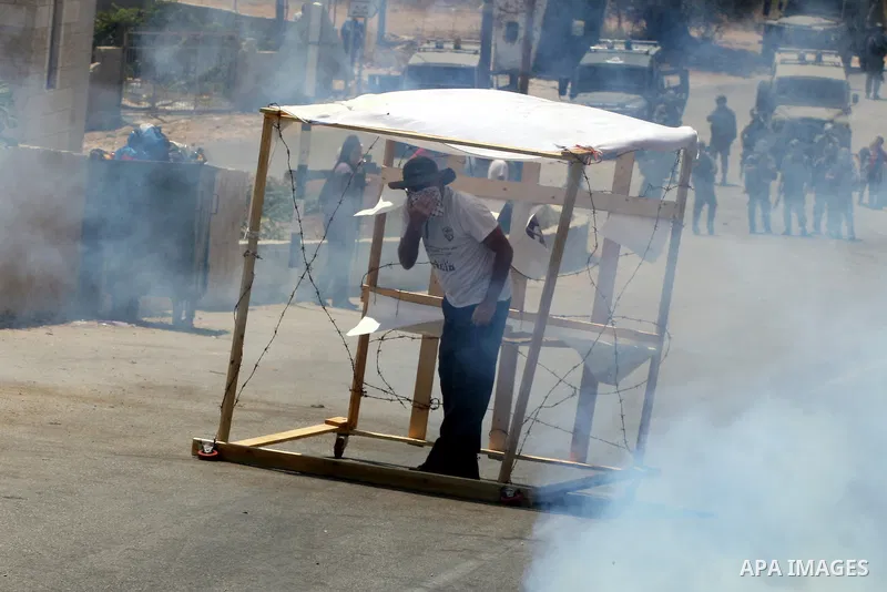 Palestinian protestors take cover from tear gas canisters fired by Israeli soldiers during clashes following a demonstration against Israeli occupation and settlements expansion, on July 15, 2011 in the West Bank village...