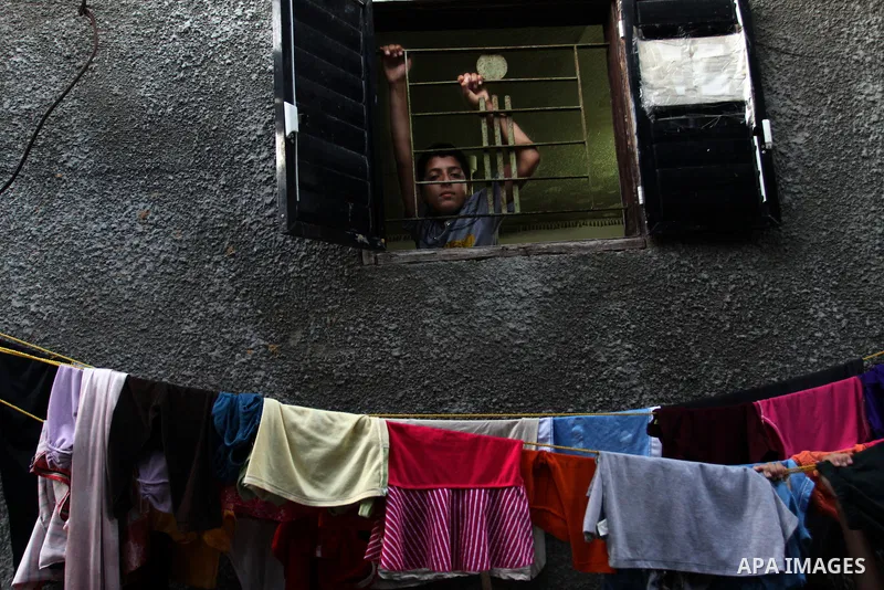 A Palestinian boy looks out from her house window in the Jabaliya refugee camp in the northern area of the Gaza Strip on July 21, 2011. The UN Relief and Works Agency (UNRWA) will reduce some of its services for Palestin...