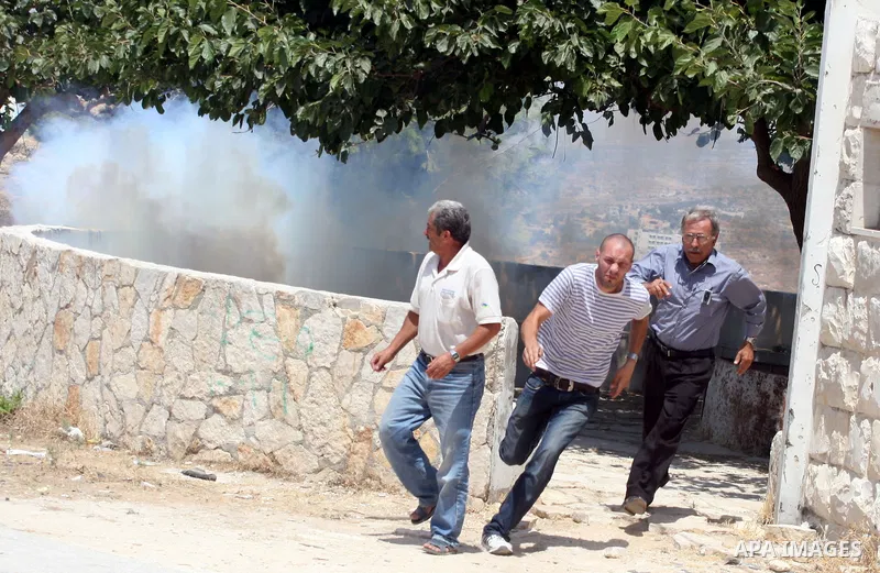 Palestinian protesters run for cover from tear gas canisters fired by Israeli soldiers in the West Bank village of Nabi Saleh, north of Ramallah, on July 22, 2011 during a weekly Friday protest against Israeli West Bank...