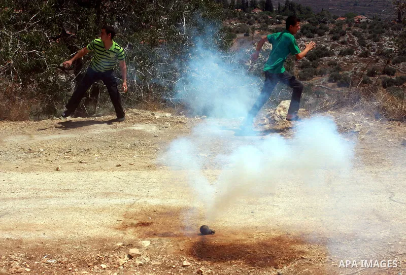 Palestinian protestors run for cover from tear gas canisters fired by Israeli soldiers during a demonstration against the closure of a road during the second Intifada by Jewish settlers from the nearby settlement of Kadu...