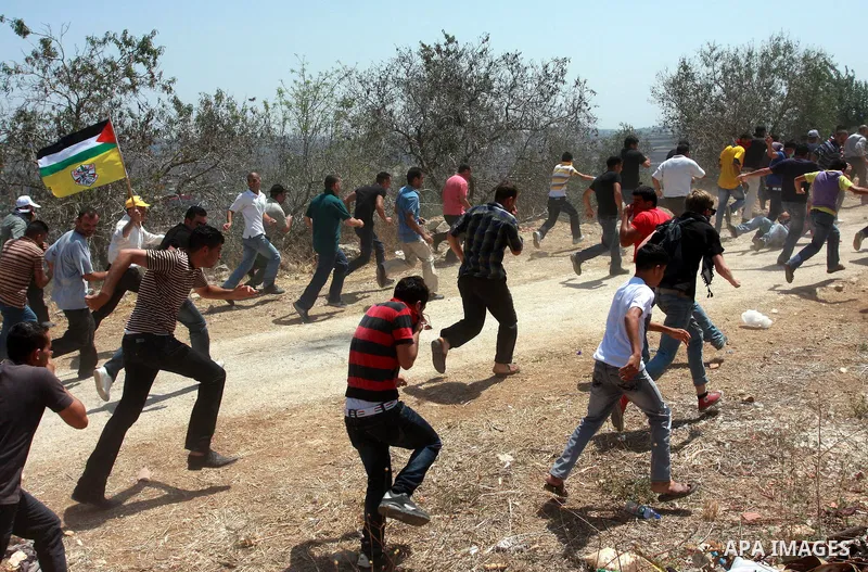 Palestinian protestors run for cover from tear gas canisters fired by Israeli soldiers during a demonstration by against the closure of a road during the second Intifada by Jewish settlers from the nearby settlement of K...