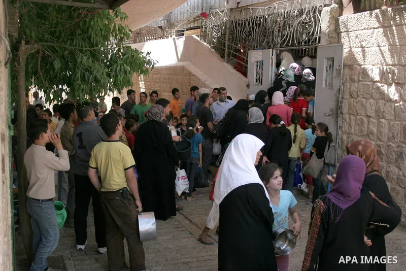 Palestinian families carry containers as they wait to receive free food for 'Iftar', the meal that breaks the daily fast during Ramadan, at an Islamic Council charity in the centre of the West Bank city of Hebron on Augu...