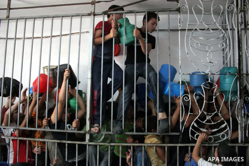 Palestinian families carry containers as they wait to receive free food for 'Iftar', the meal that breaks the daily fast during Ramadan, at an Islamic Council charity in the centre of the West Bank city of Hebron on Augu...