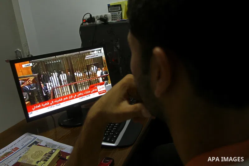 Palestinians watch the video image taken from Egyptian State Television shows 83-year-old Hosni Mubarak laying on a hospital bed inside a cage of mesh and iron bars as he flanked by his sons Alaa, left, and Gamal right,...