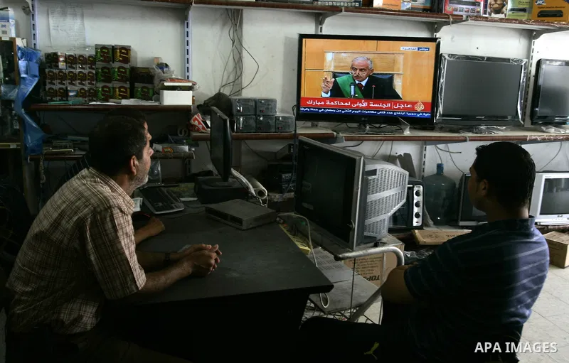 Palestinian men watch the video image taken from Egyptian State Television at a shop in Rafah, southern Gaza Strip, where shows 83-year-old Hosni Mubarak laying on a hospital bed inside a cage of mesh and iron bars as he...