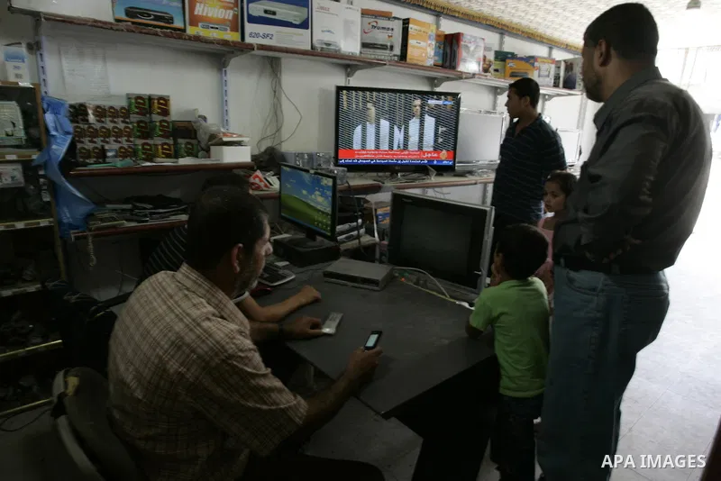 Palestinian men watch the video image taken from Egyptian State Television at a shop in Rafah, southern Gaza Strip, where shows 83-year-old Hosni Mubarak laying on a hospital bed inside a cage of mesh and iron bars as he...