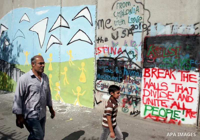 Palestinians walk past a mural painted on a section of the controversial Israeli barrier near an Israeli checkpoint to Jerusalem in the West Bank city of Bethlehem during the first Friday of the holy month of Ramadan Aug...