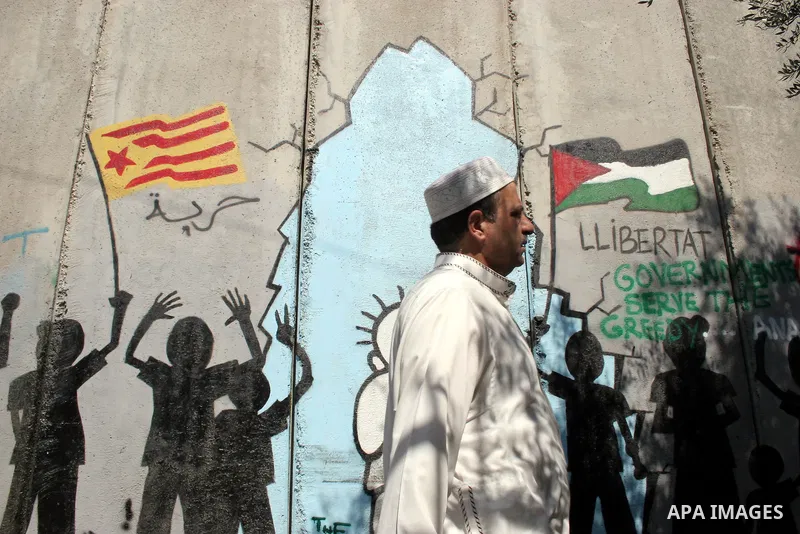 A Palestinian man walks past a mural painted on a section of the controversial Israeli barrier near an Israeli checkpoint to Jerusalem in the West Bank city of Bethlehem during the first Friday of the holy month of Ramad...