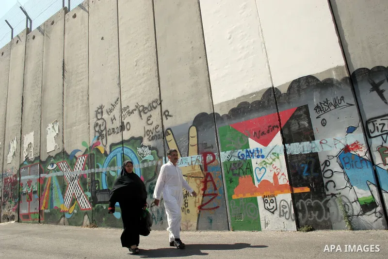 Palestinians walk past a mural painted on a section of the controversial Israeli barrier near an Israeli checkpoint to Jerusalem in the West Bank city of Bethlehem during the first Friday of the holy month of Ramadan Aug...