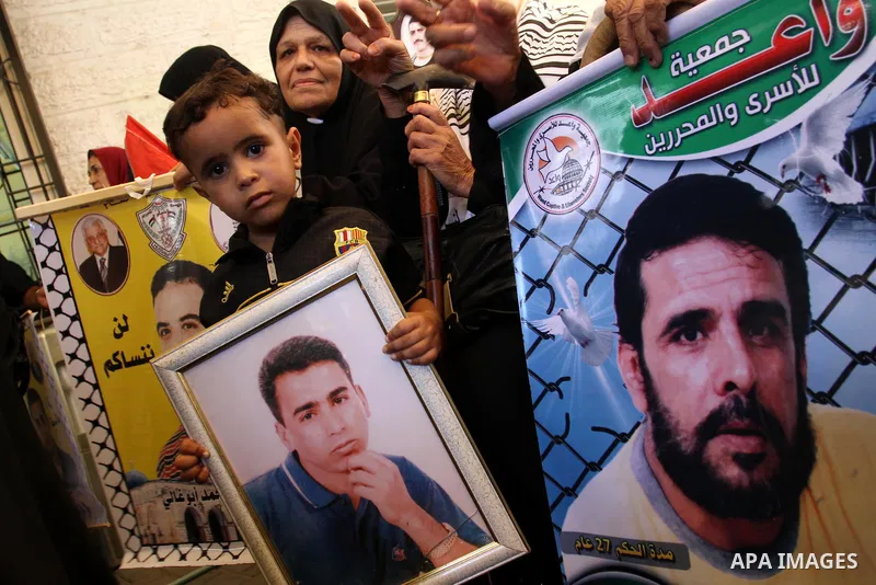 A Palestinian boy with his mother hold pictures of their prisoned relatives in Israeli jails as they gather in a weekly activity calling for their liberty at the Red Cross headquarters in Gaza City on Aug. 8, 2011. About...