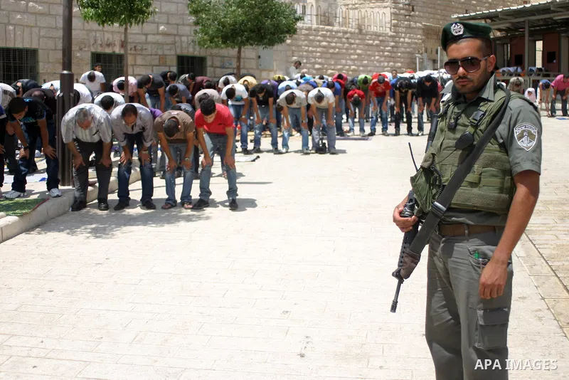 An Israeli soldier stands guard as Palestinians perform the second friday prayer of Islam's holy fasting month of Ramadan outside the Ibrahimi mosque, or the Tomb of the Patriarchs, in the divided West Bank city of Hebro...