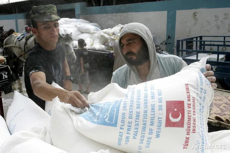 A Palestinian man carries a bag with wheat flour on his shoulders as others receive food aids from the United Nations Relief and Works Agency (UNRWA) at the Rafah refugee camp, in the southern Gaza Strip on August 15, 20...